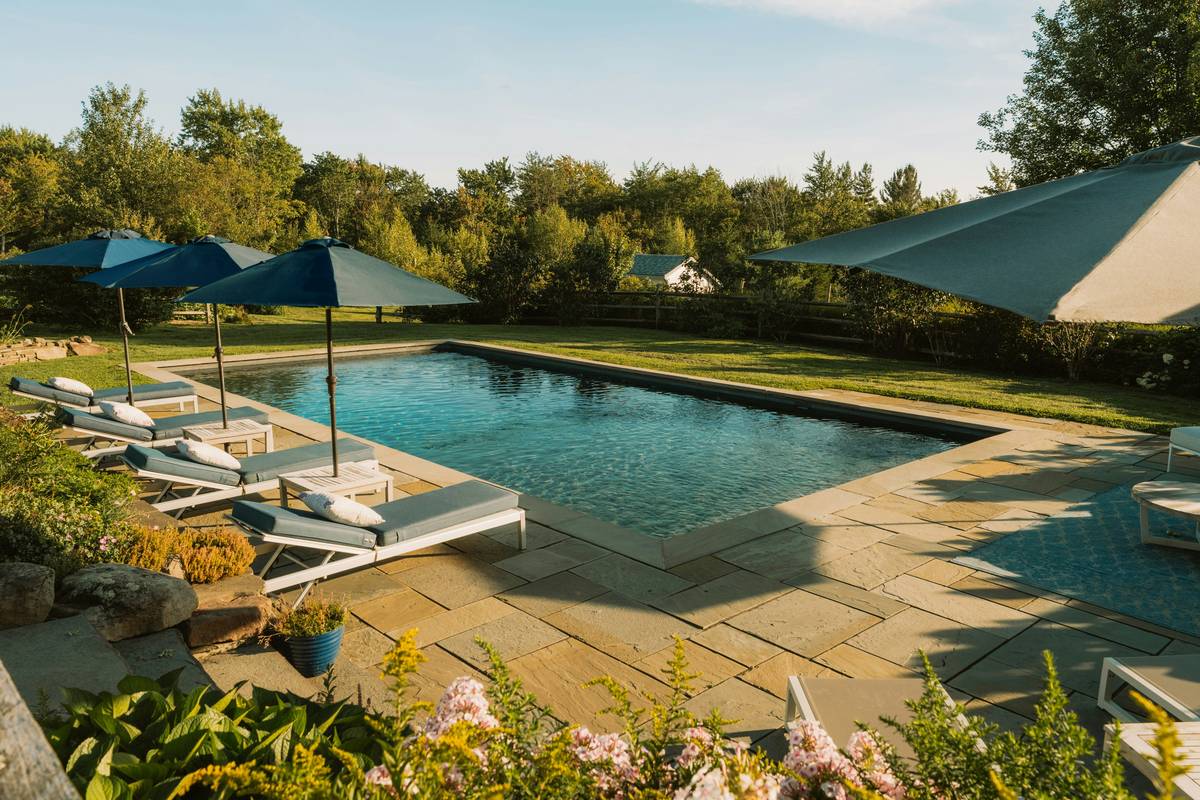 Sturdy poolside umbrellas with stand providing shade over lounge chairs by backyard pool